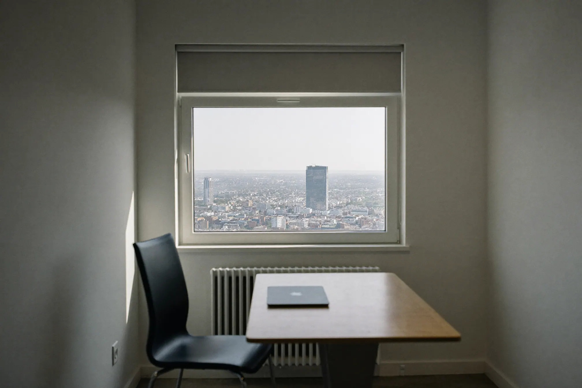 A small, tidy private office with a pale oak desk, one dark chair and a large window with a soft city view