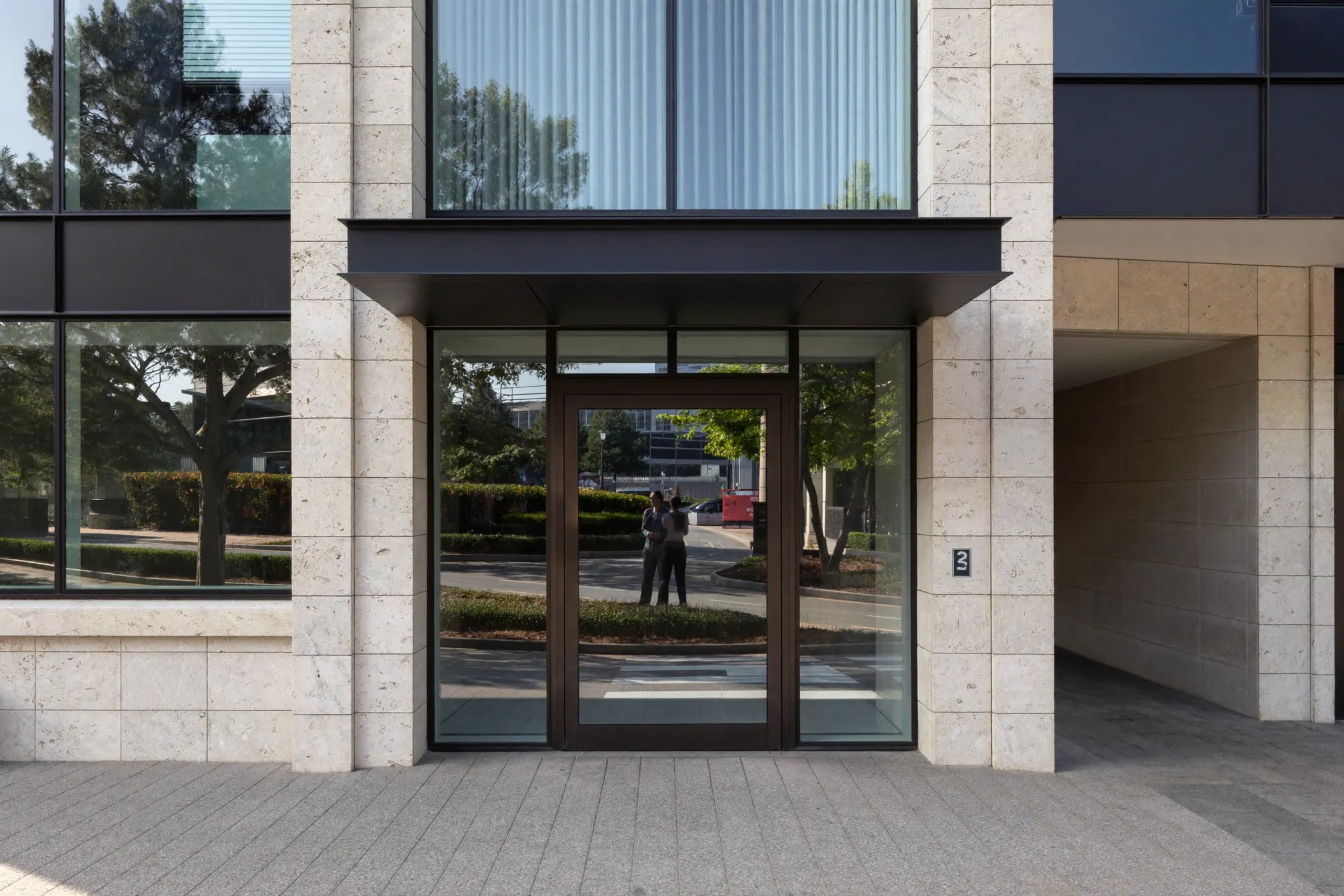 The glass entrance of a modern mid-rise office building on a quiet street in the morning