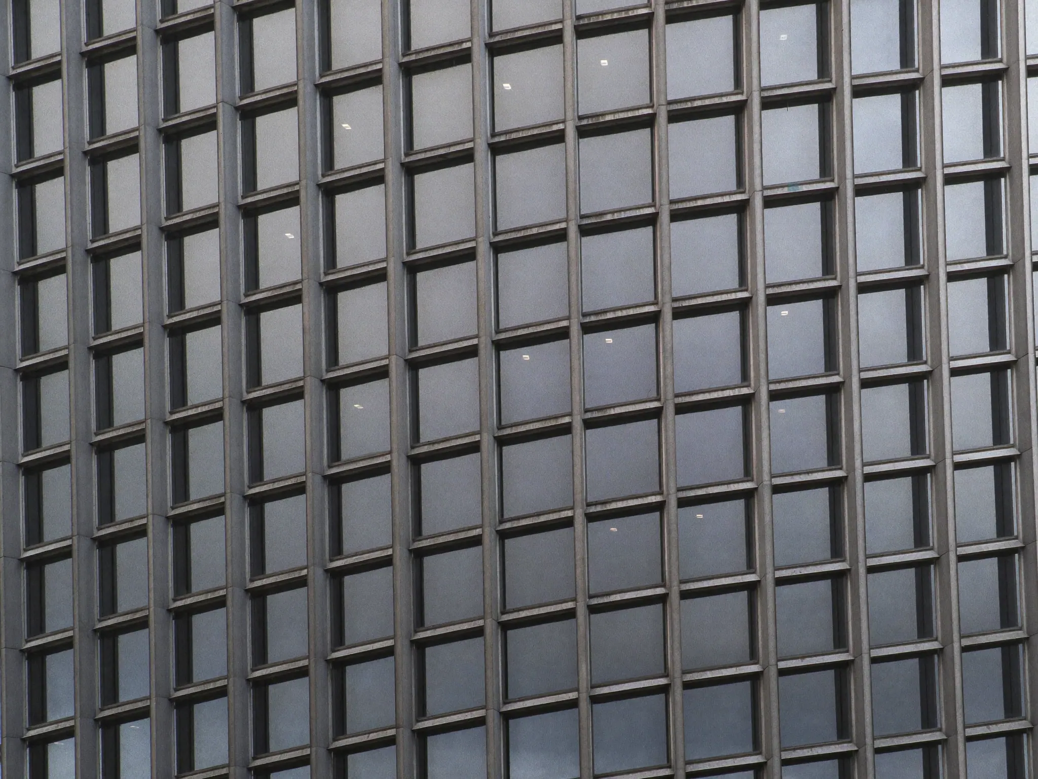 Looking up at the glass and steel grid of an office tower facade under an overcast sky